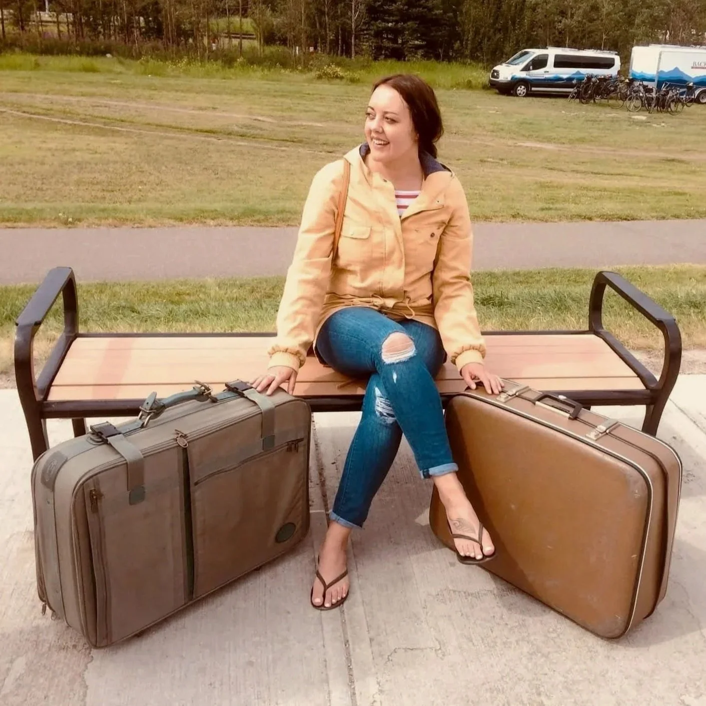 A woman with dark hair, light skin, and green eyes, wearing a beige sweater, standing in front of a plain light-colored wall.