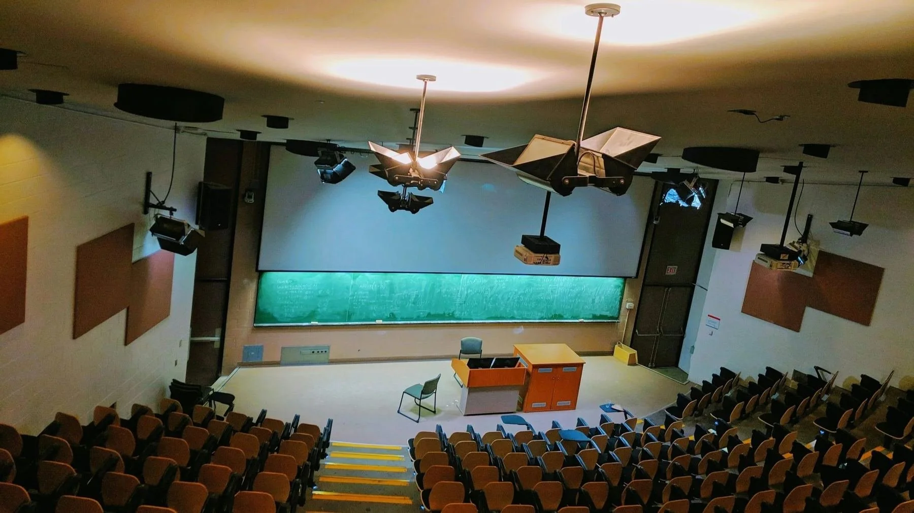 Tiered lecture theatre with ceiling-mounted projectors and speakers above rows of seating