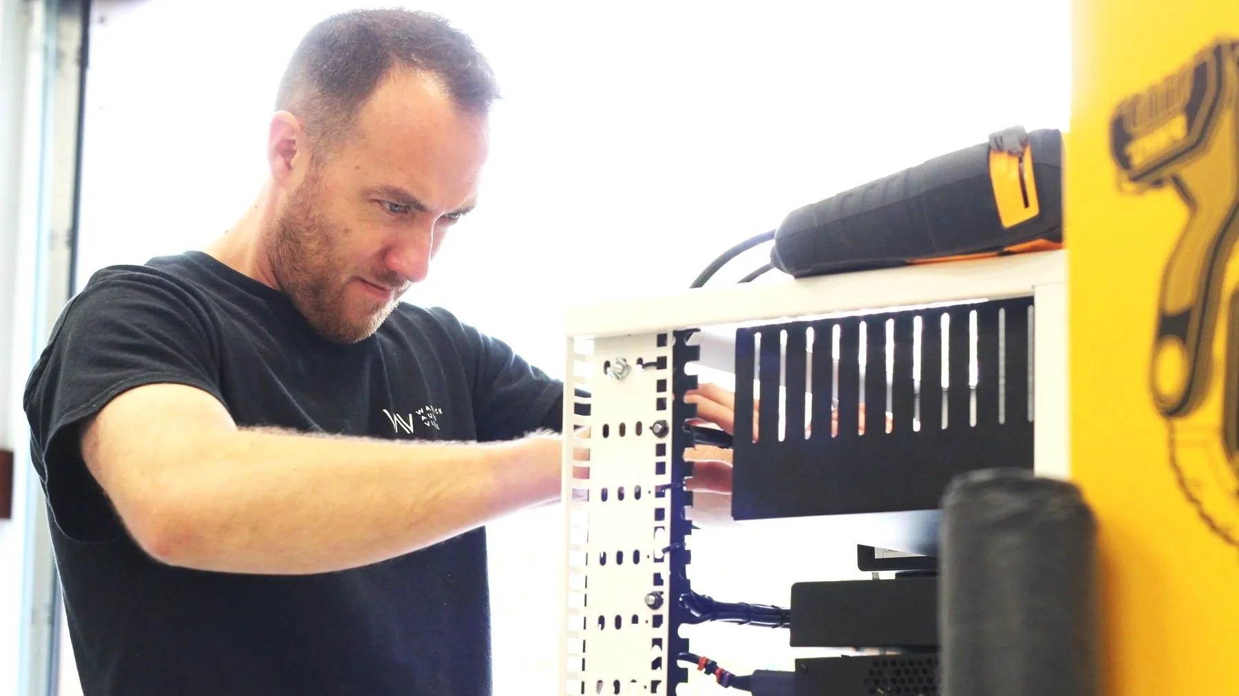 Technician in a Warwick AV T-shirt wiring an open equipment rack