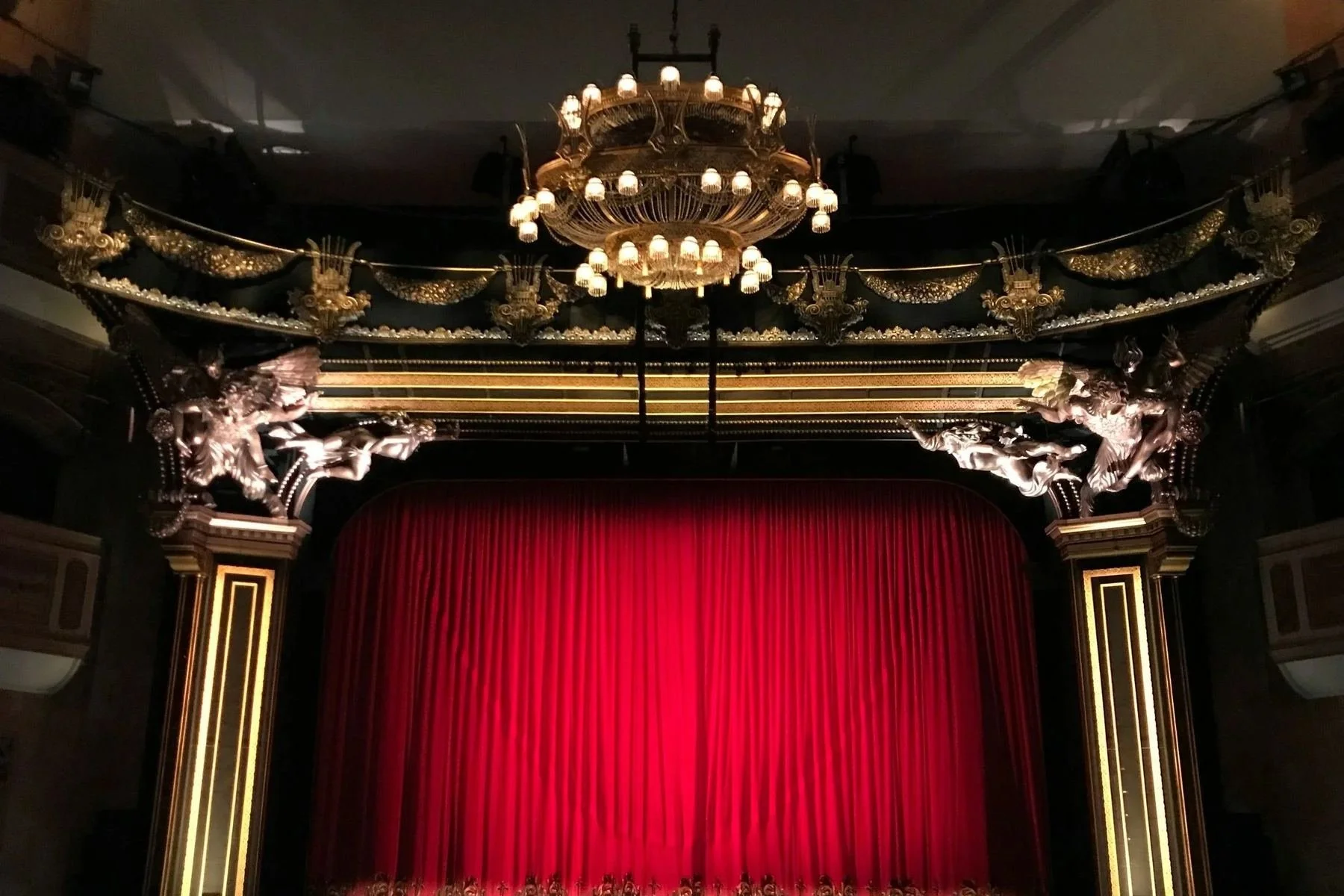 Theatre stage with a red curtain, ornate gilded proscenium arch and chandelier
