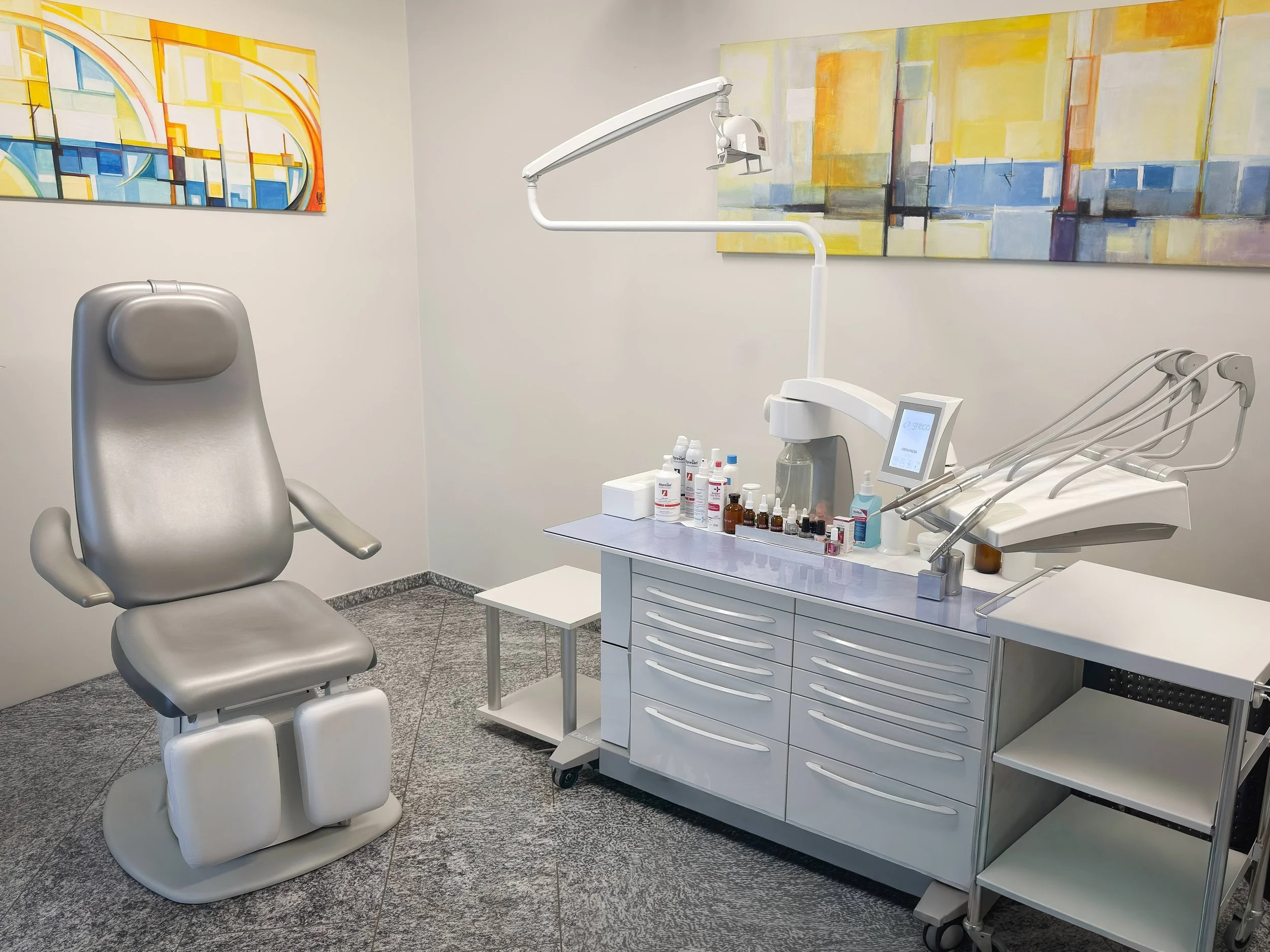 Ein Behandlungsstuhl in einer Podologiepraxis mit medizinischen Instrumenten und Behandlungsutensilien auf einer weissen Kommode, Wandkunst an der Wand.