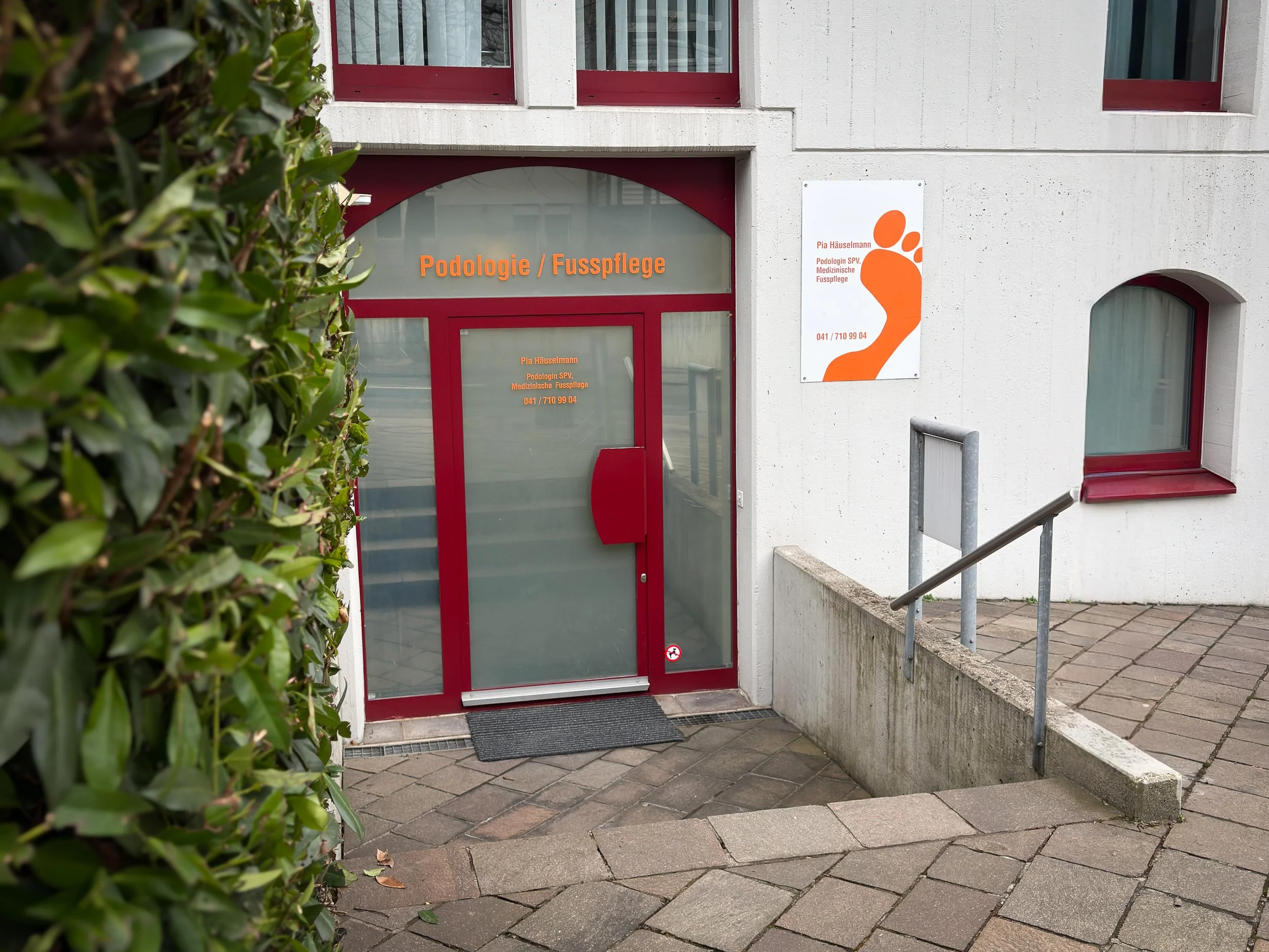 Außenansicht eine Podologiepraxis. Es gibt einen Schild mit einer orangen Fußtkontur und dem Namen der Podologin.