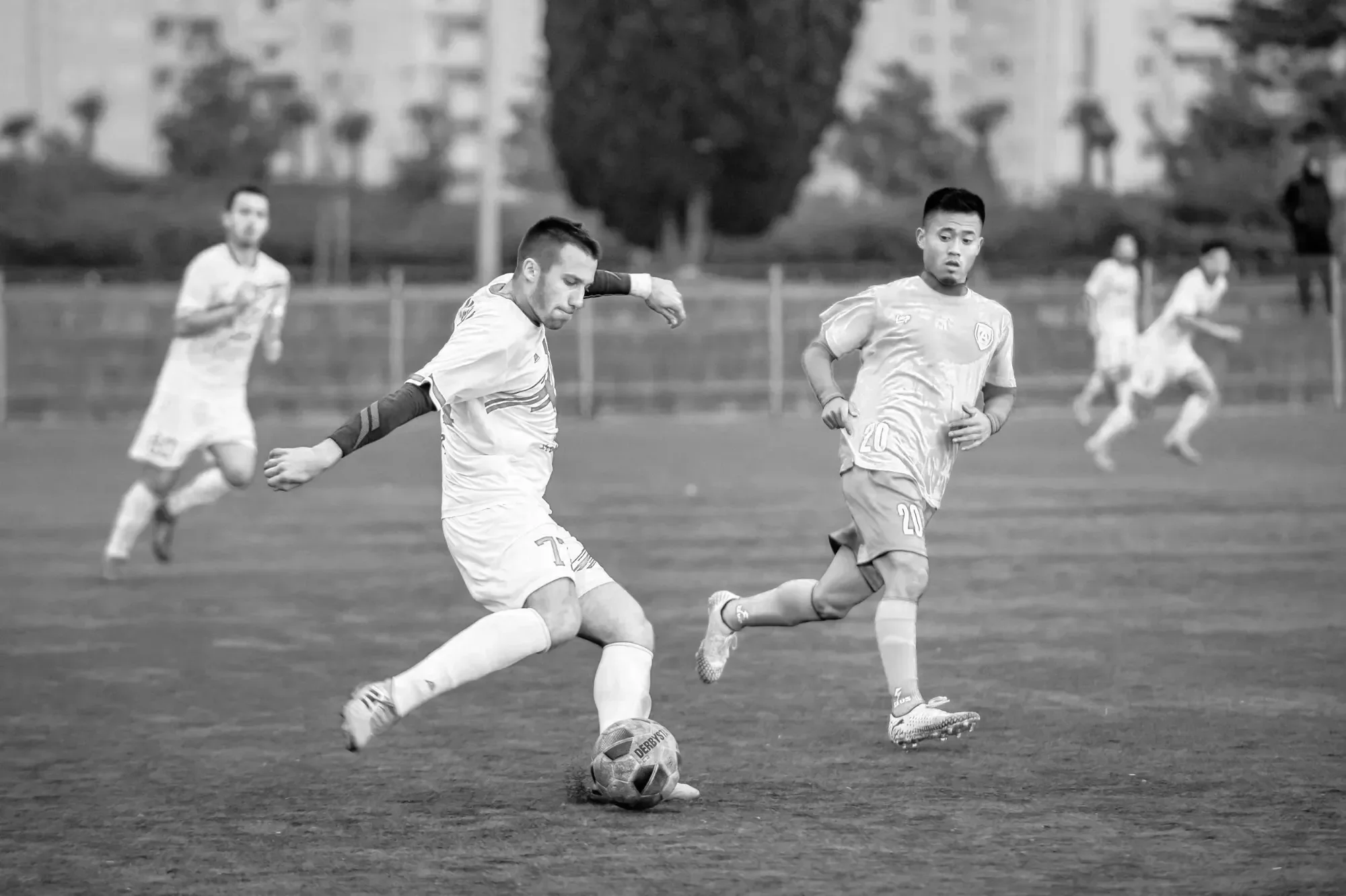 A black and white photo of soccer players on the field, with one player kicking the ball while others run behind him.