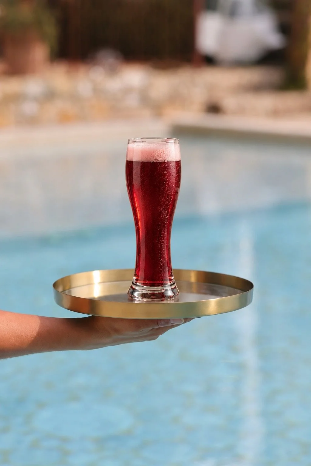 Schooner glass of Gold Coast cherry beer served on a round tray over a swimming pool