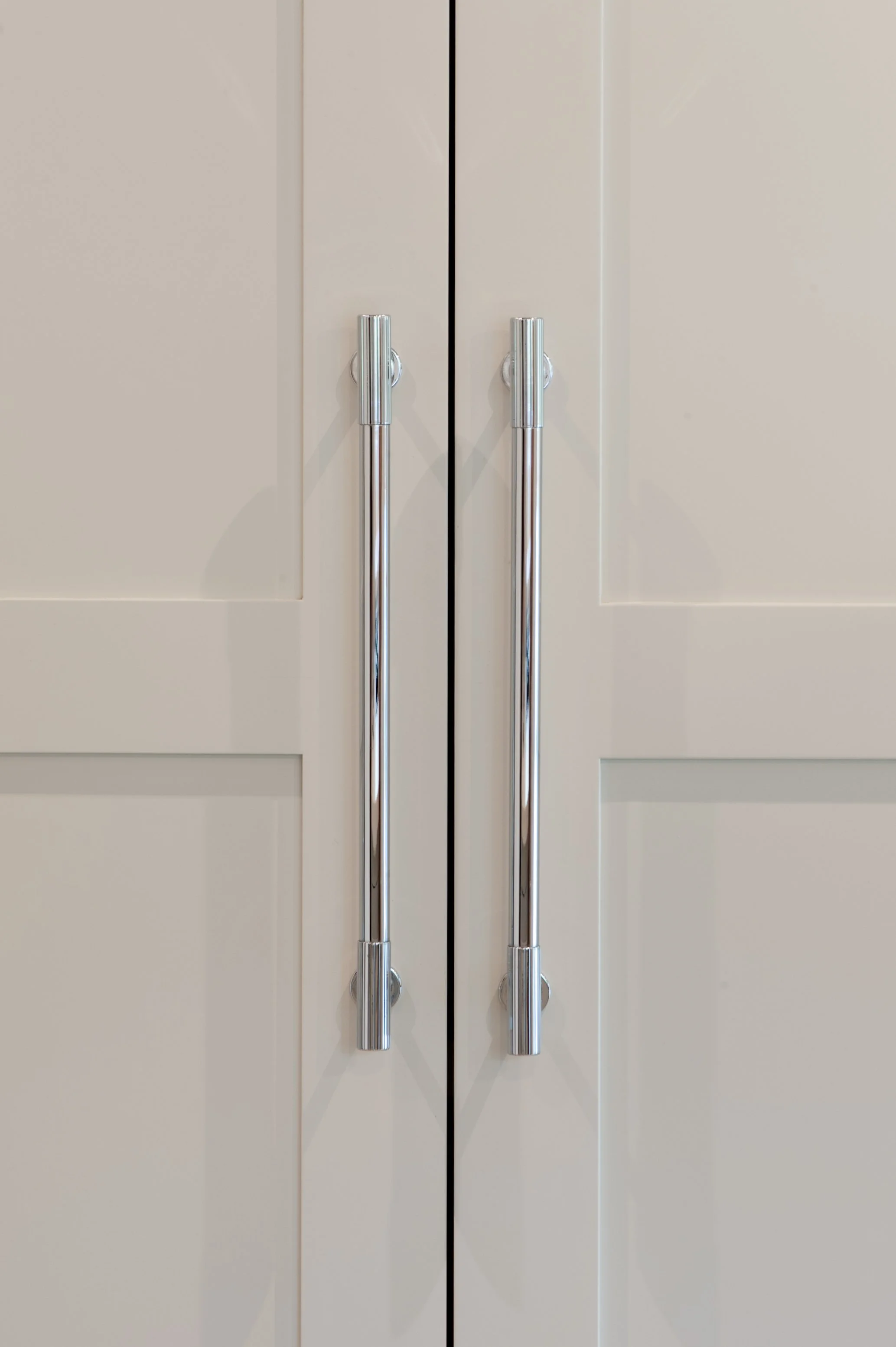 Close-up of beige kitchen cabinet doors with silver vertical handles.