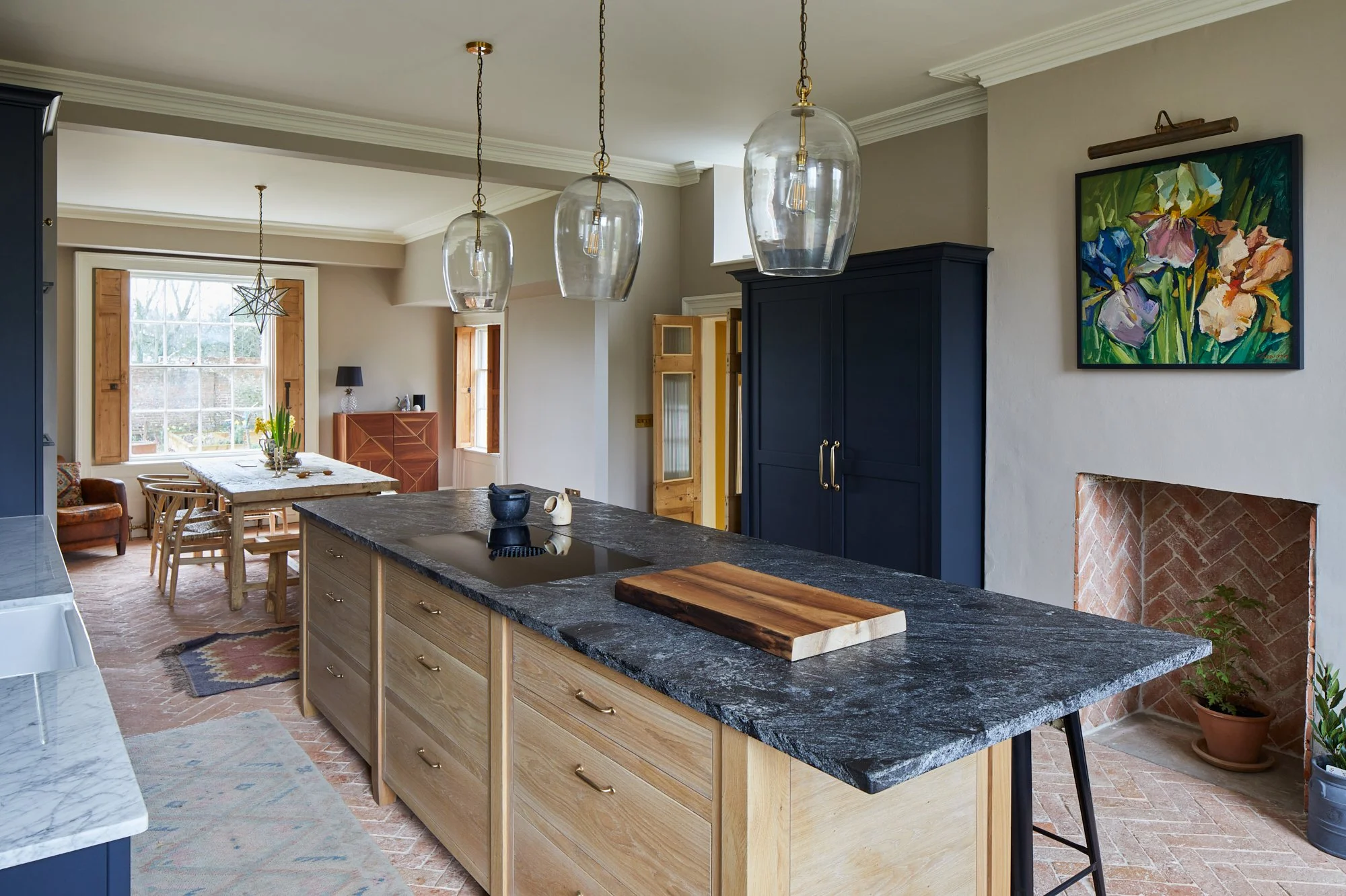 Modern kitchen with black granite countertop island, light wood cabinets, hanging glass pendant lights, and colorful floral artwork on the wall.