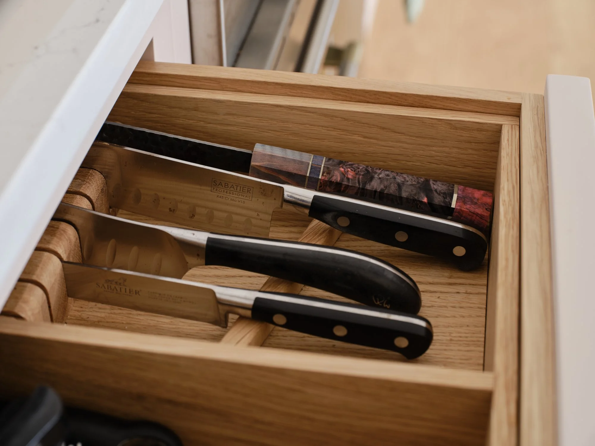 A wooden knife drawer with knives, including one with a black handle and white polka dots, stored inside.