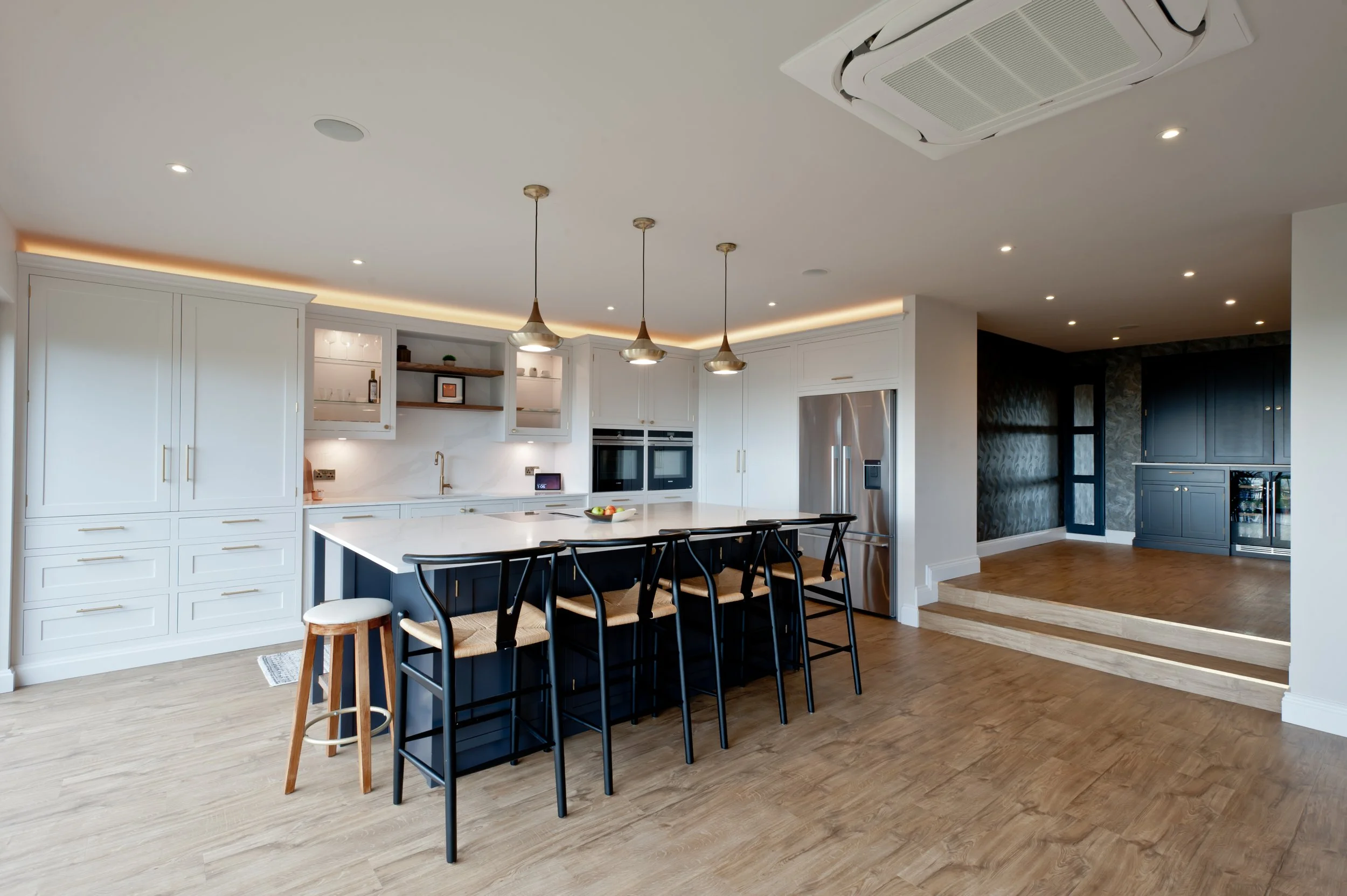 Modern kitchen with white cabinets, a large island, black chairs, pendant lighting, and wooden flooring.