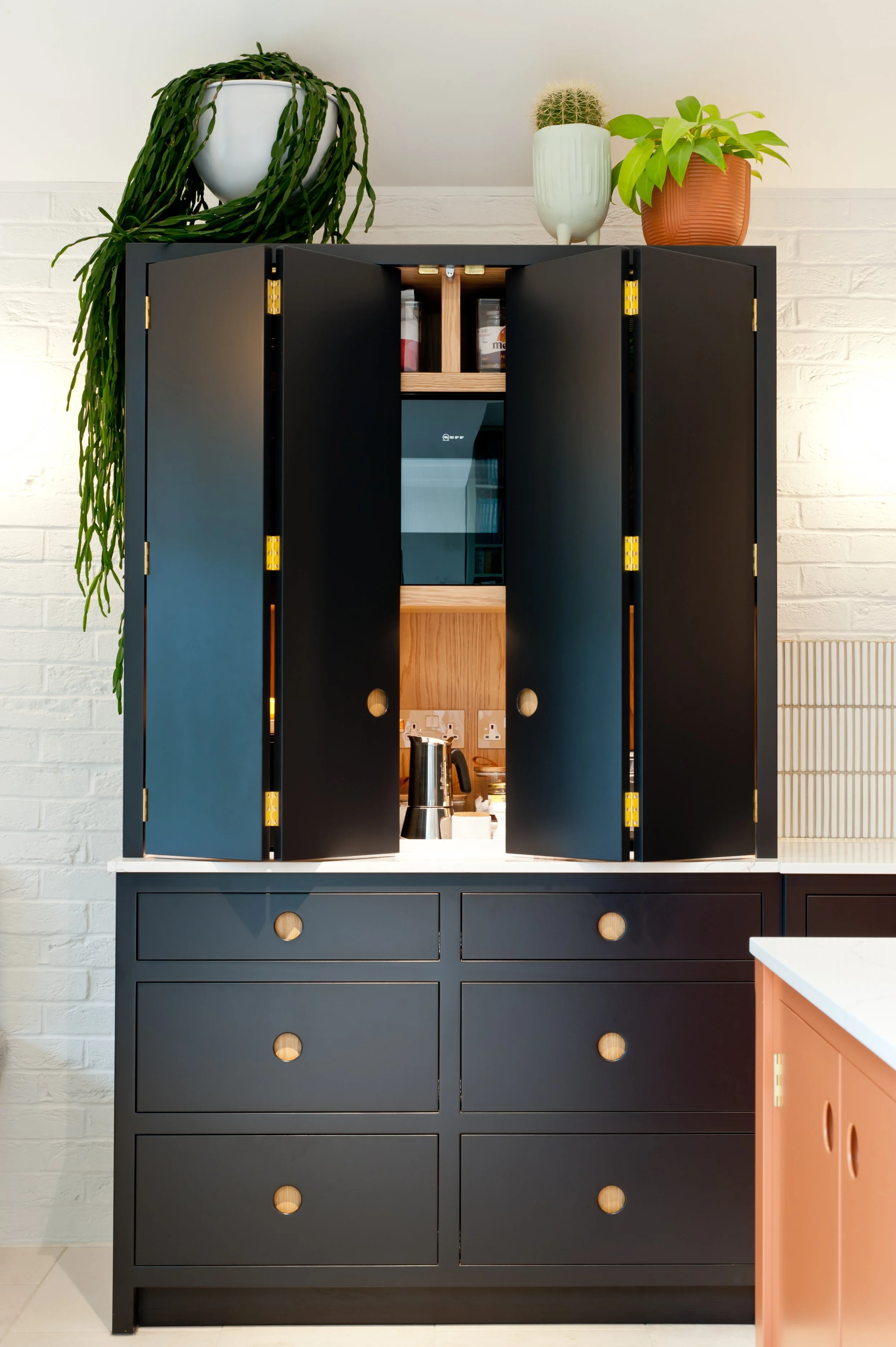 Open Off-Black bespoke kitchen cabinet revealing oak shelving, concealed appliances and brass hinges at Cornwall Gardens, Margate.