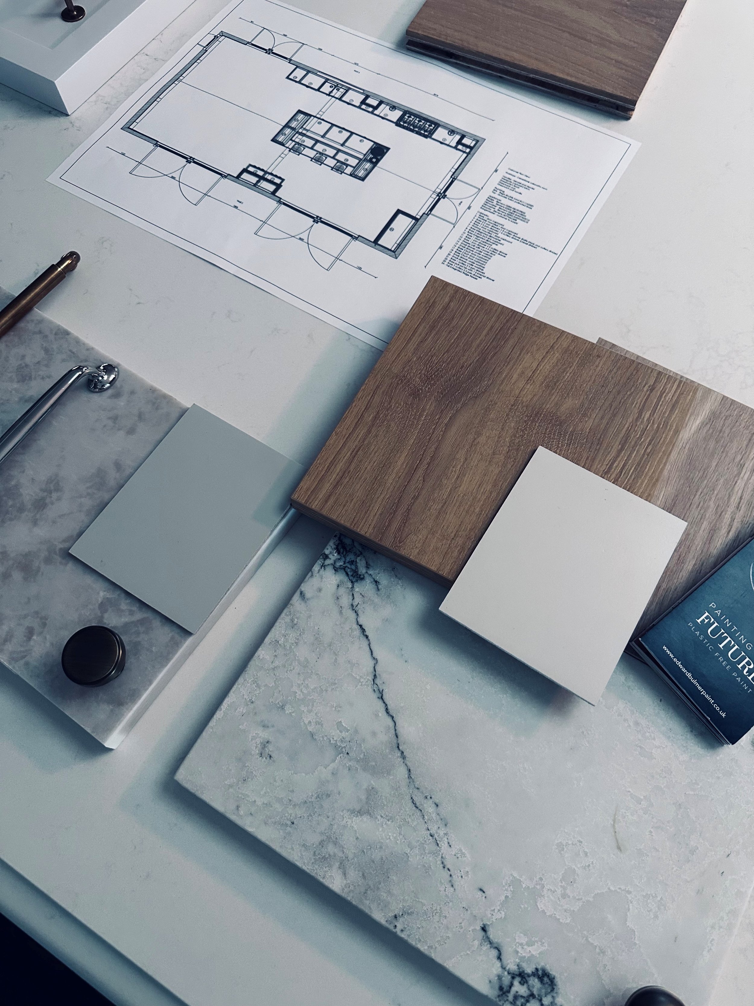 Architectural floor plan on a white marble table with wood samples nearby.