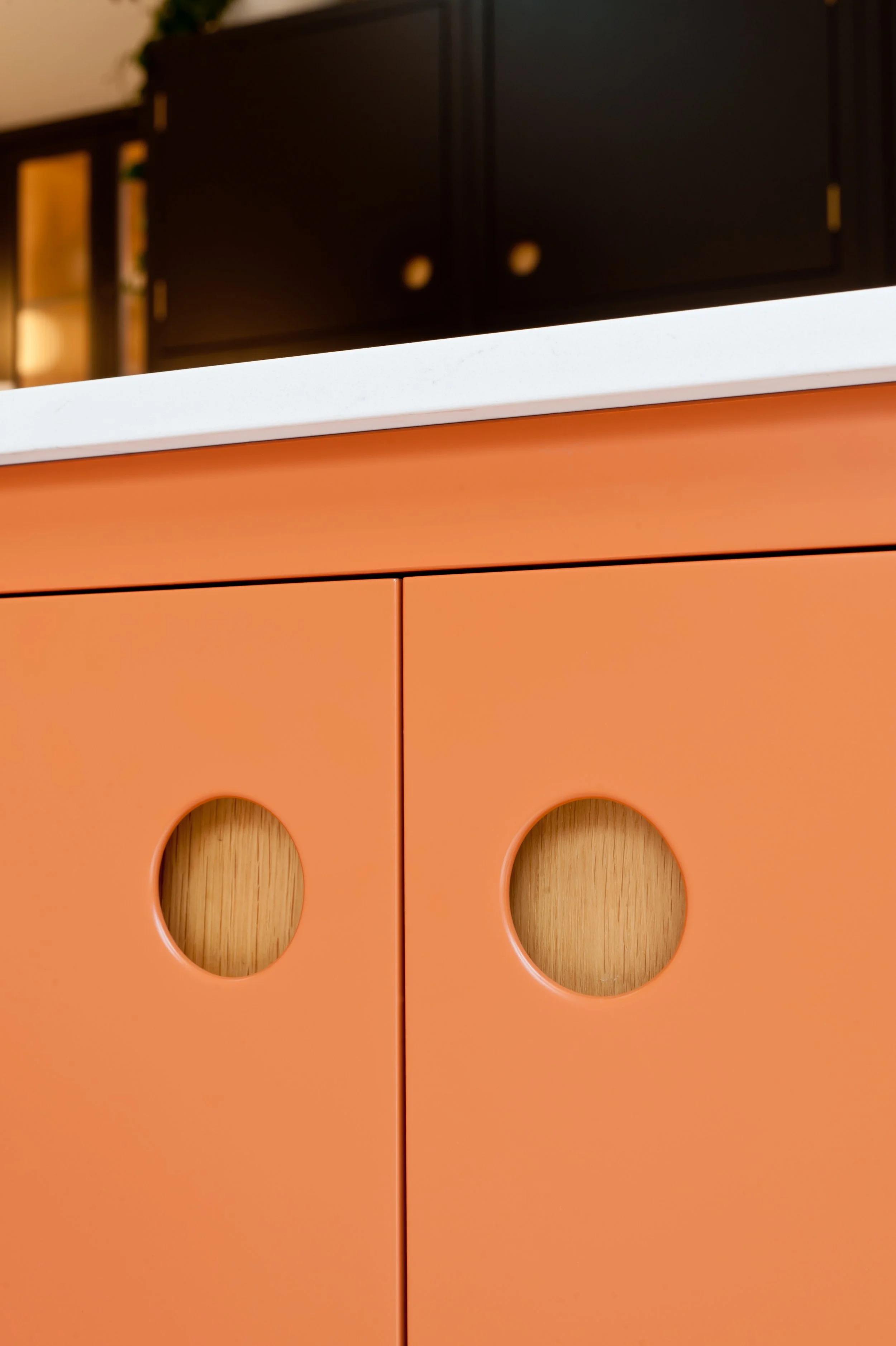 Close-up of bespoke orange kitchen cabinet doors featuring circular cut-out handles with contrasting natural oak backs.