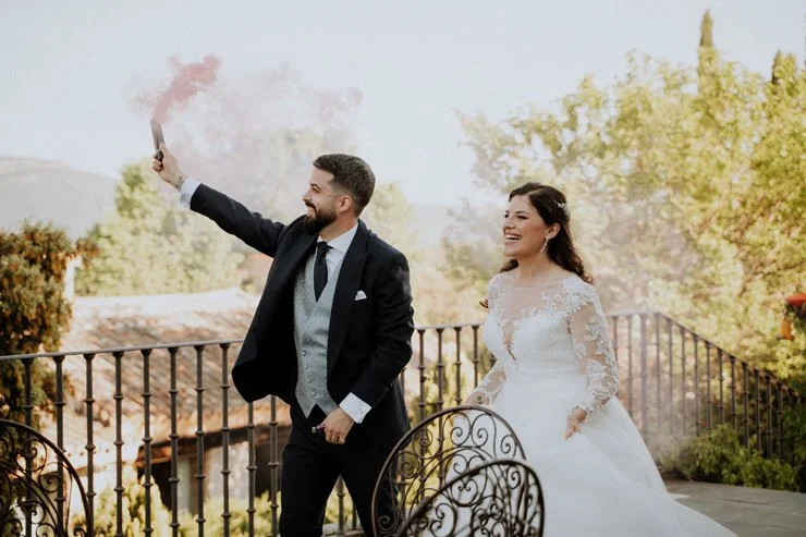 fotografía pareja de recién casados en una terraza, el hombre sostiene una bengala con humo rosa y ambos sonríen, con árboles y una montaña al fondo, Madrid, Raquel Botas.