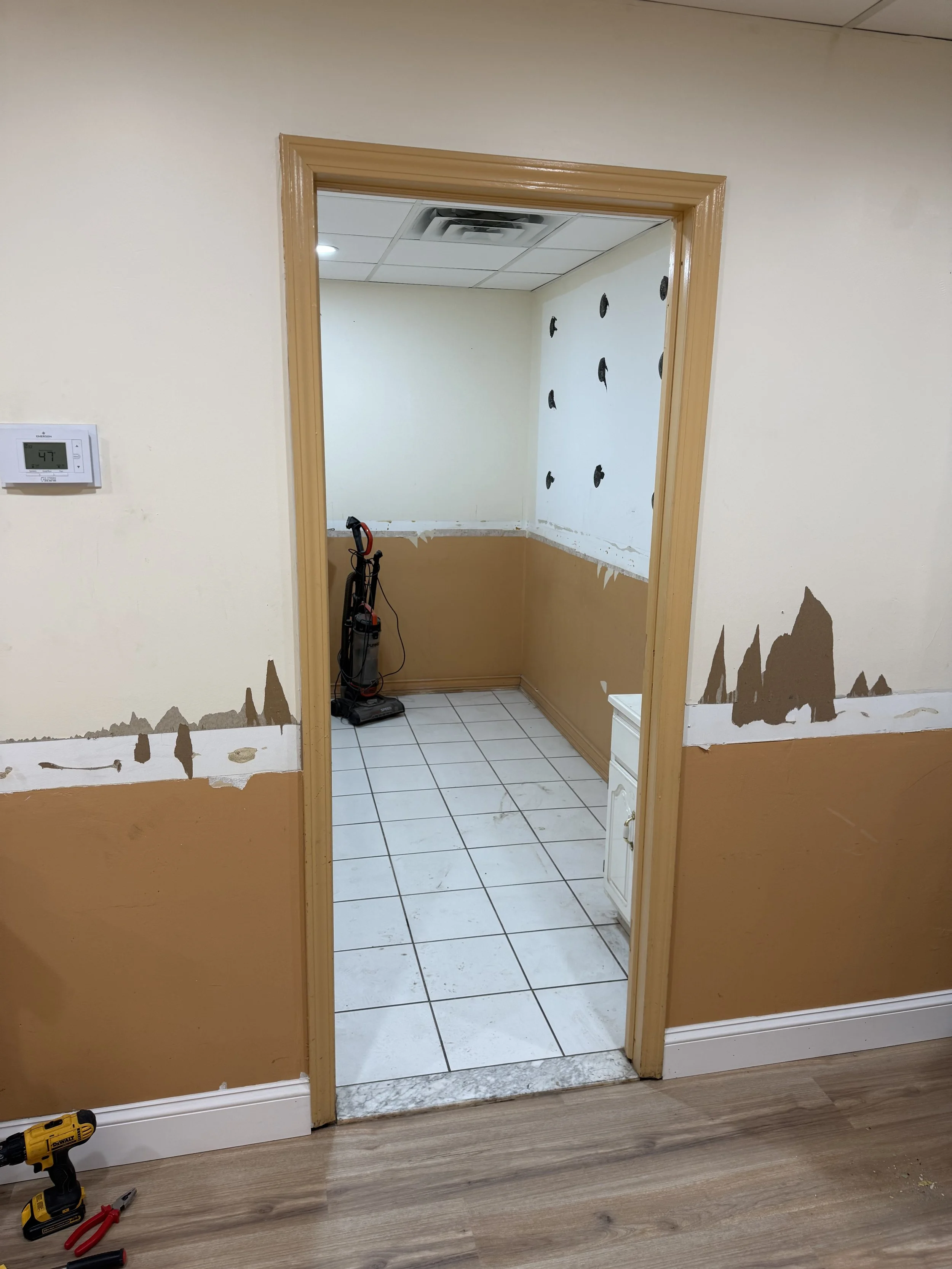 Kitchen area under renovation with partially removed wallpaper, a vacuum cleaner, and a small cabinet.