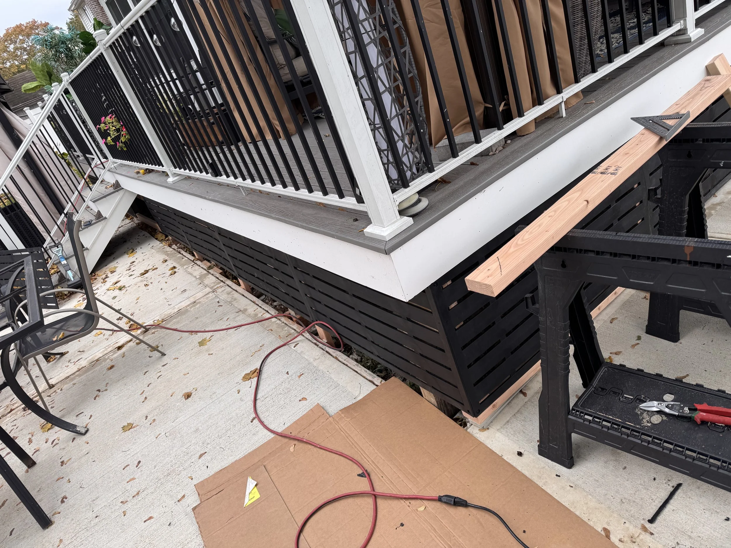 Construction work on an outdoor balcony with black railing, wooden trim, tools, and materials.