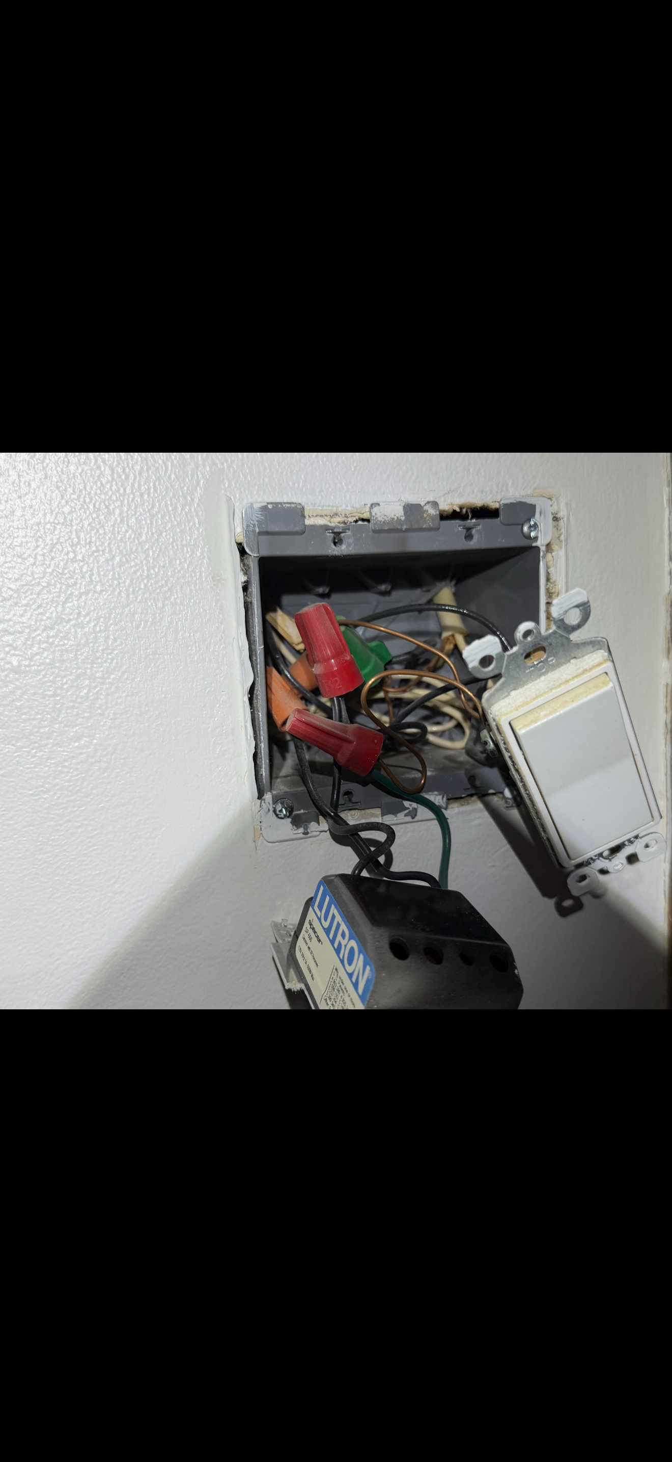 Open electrical box with tangled wires, switches, and a black component labeled "EUROON" mounted outside the box on a white wall.