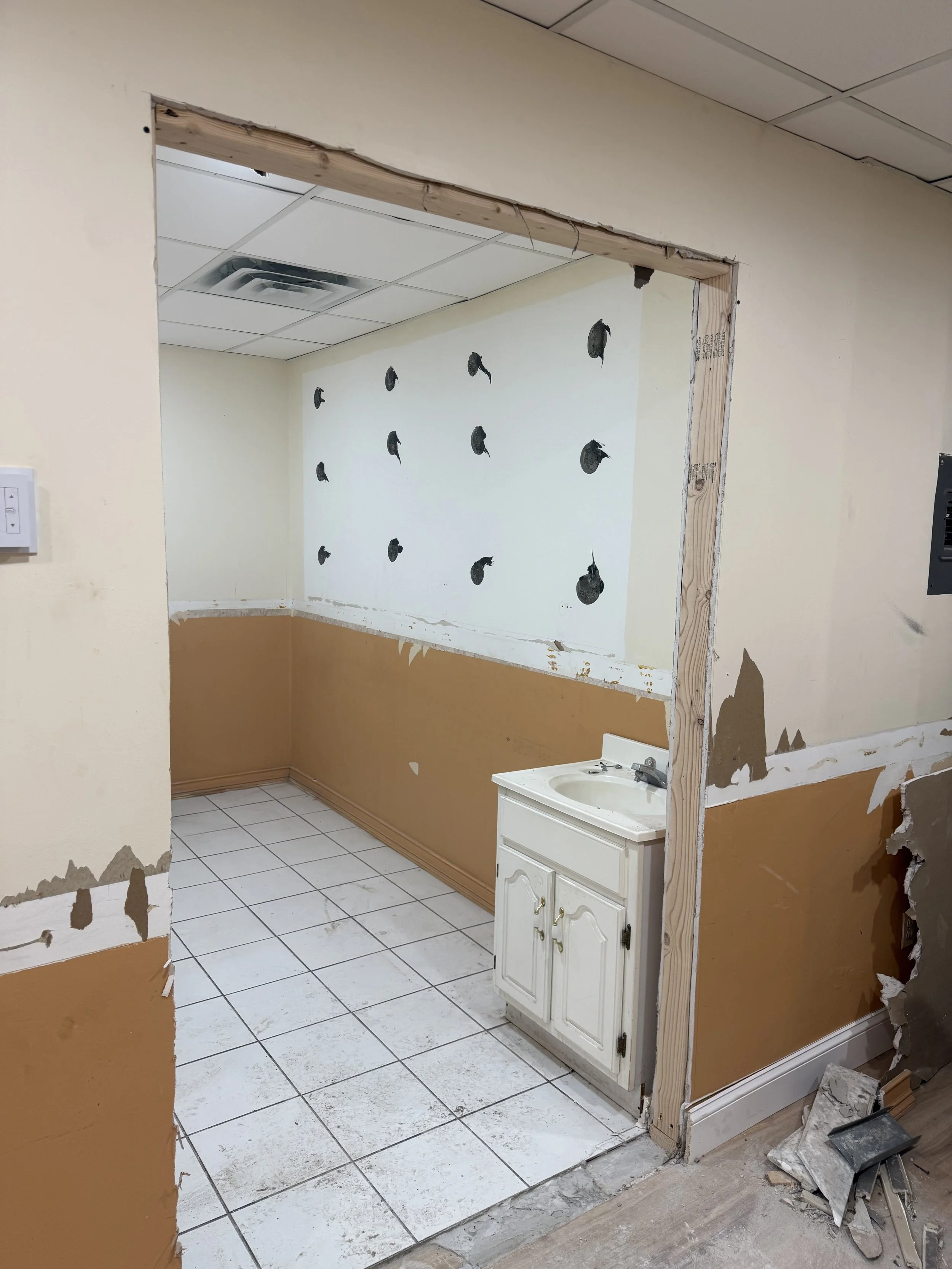 A room under renovation with hole in wall, partially removed trim, white sink cabinet, and tiled floor.