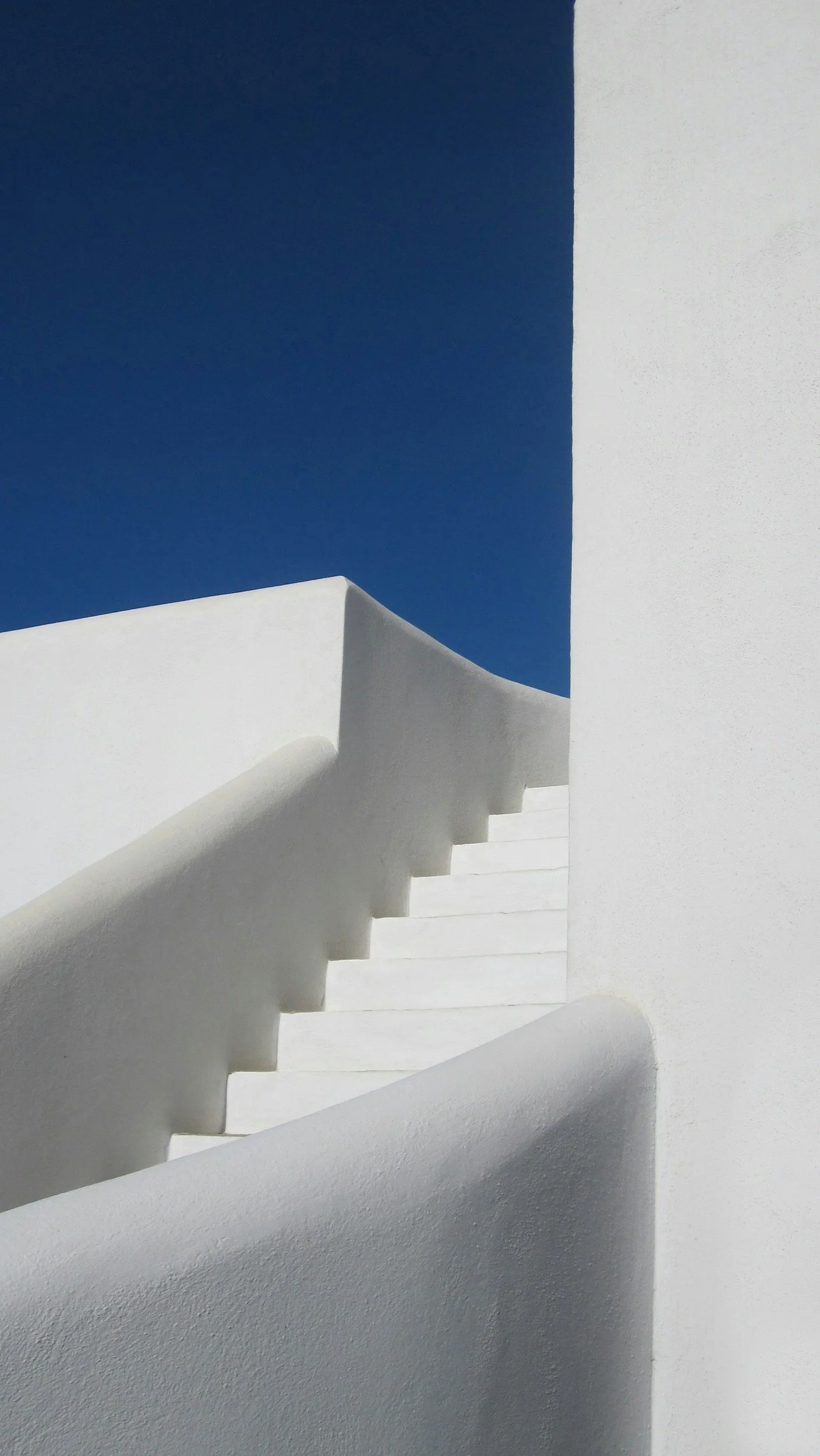 White curved staircase against a white wall with a deep blue sky in the background.