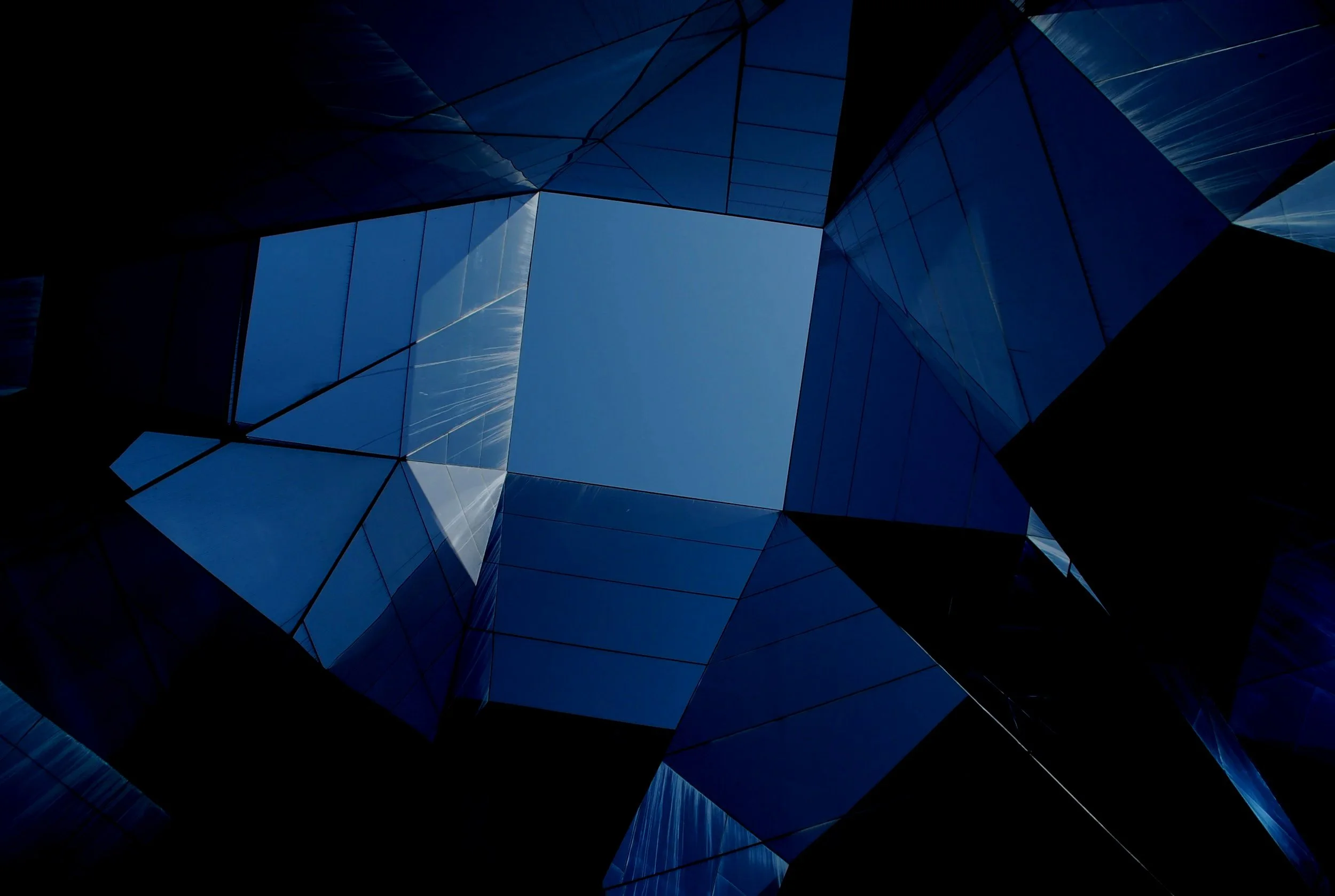 Looking up at a modern glass building with geometric shapes and reflections of the sky.