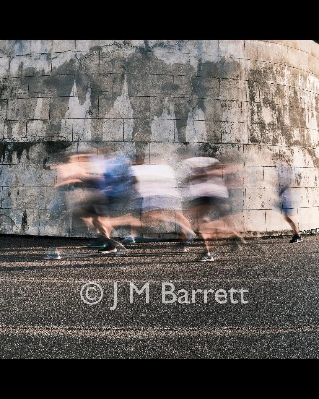Blurred motion of people walking in front of a weathered concrete wall.
