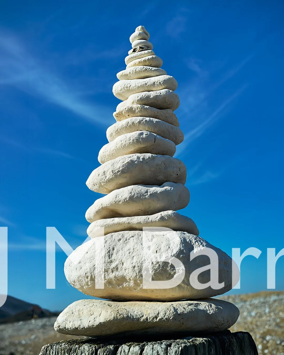 Stacked white stones balanced on a wooden post against a blue sky.