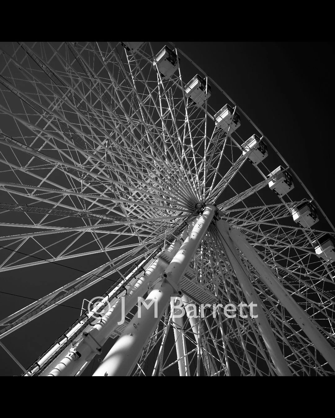 Black and white photo of a large Ferris wheel viewed from below against a dark sky.