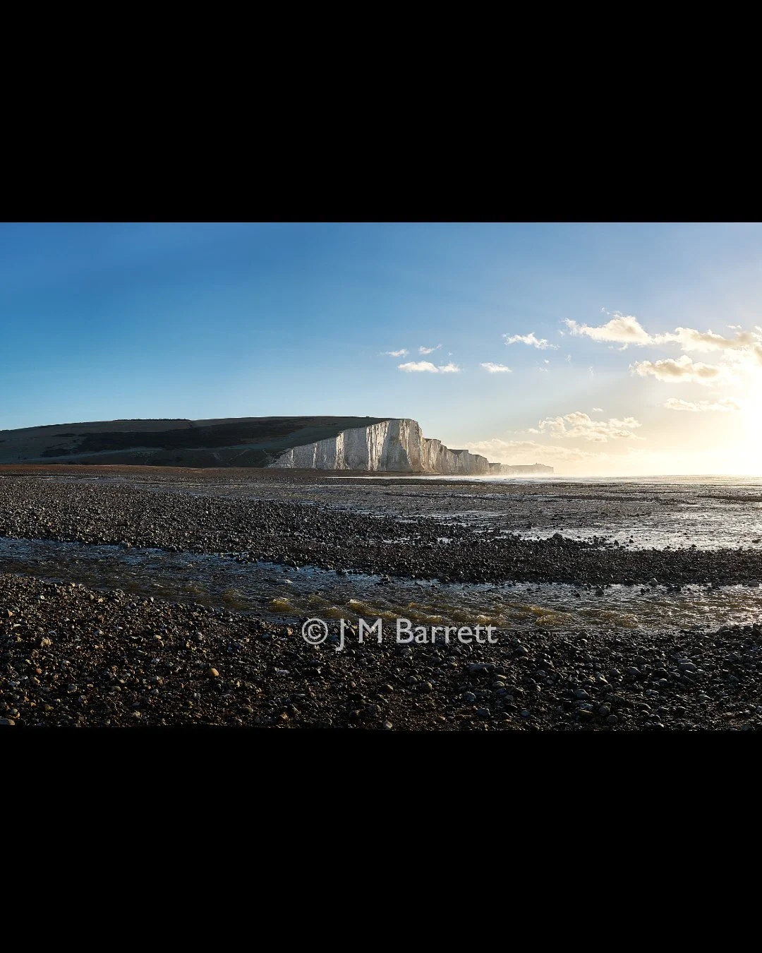 Cliffs along a coastline with a pebbled beach and the ocean during sunset