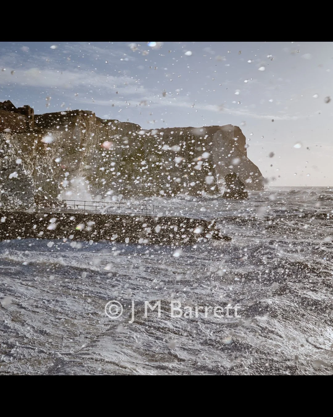 Ocean waves crashing against rocky cliffs with sea spray in the air during daytime.