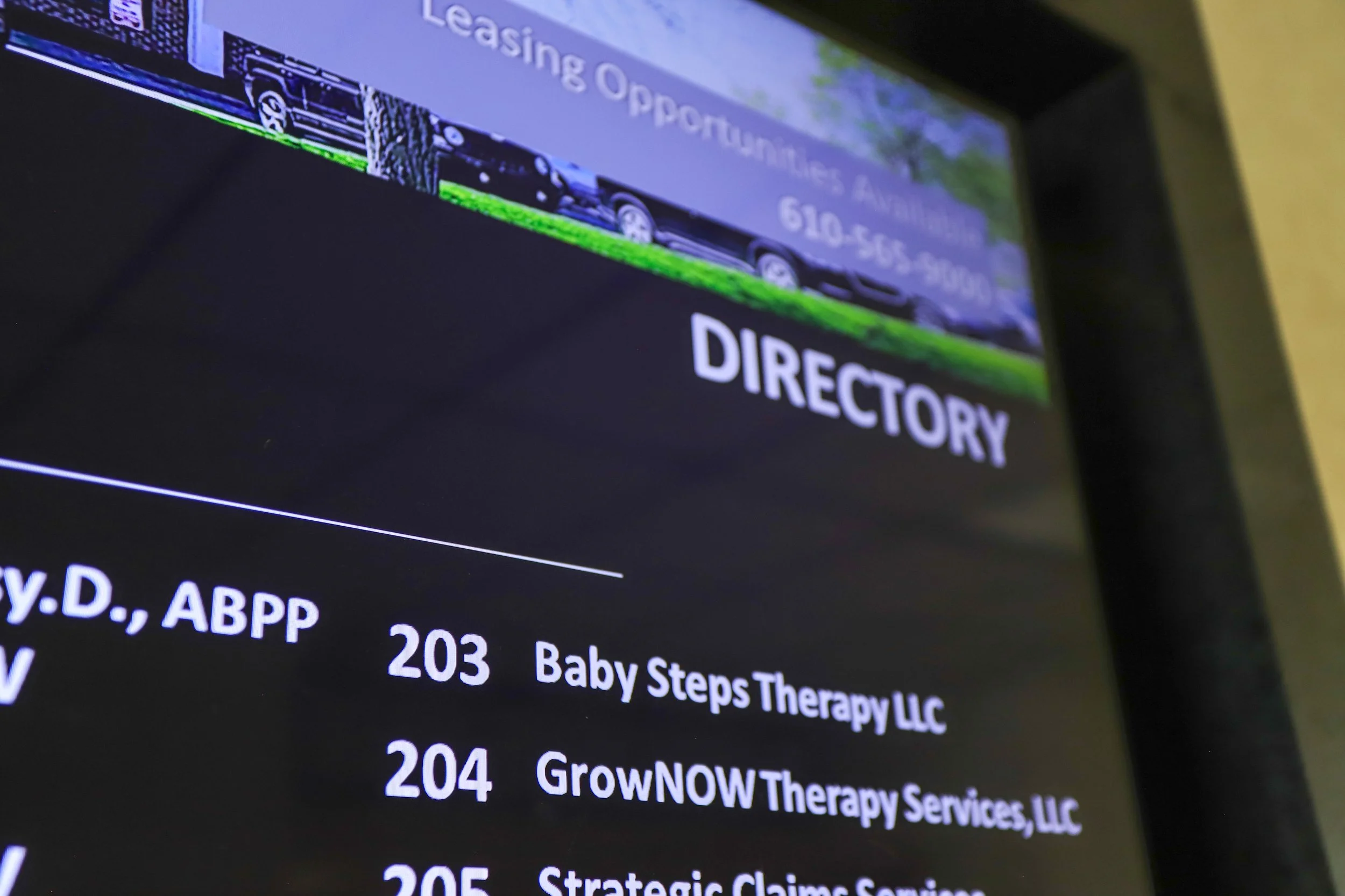 A digital directory screen displaying leasing opportunities, contact phone number, and a list of businesses including Baby Steps Therapy LLC and GrowNOW Therapy Services LLC.