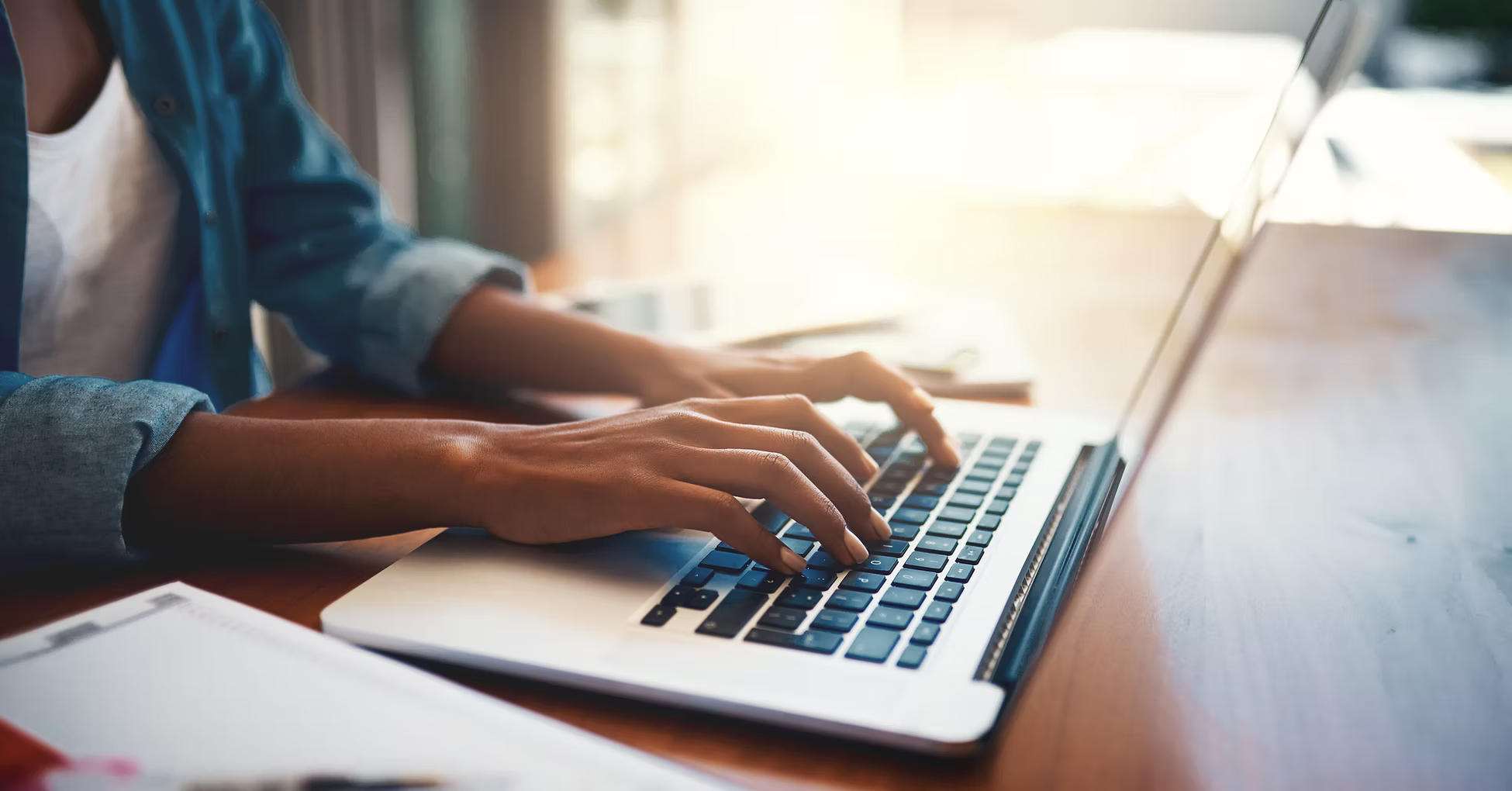 Person typing on a laptop keyboard at a wooden desk.