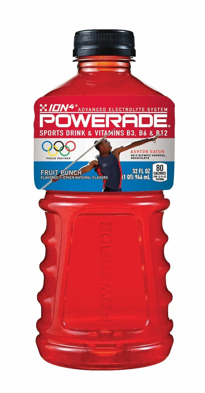 A red Powerade sports drink bottle with black cap, displaying a label with Olympic rings, a photo of a female athlete, and text indicating it is a fruit punch flavored electrolyte drink.
