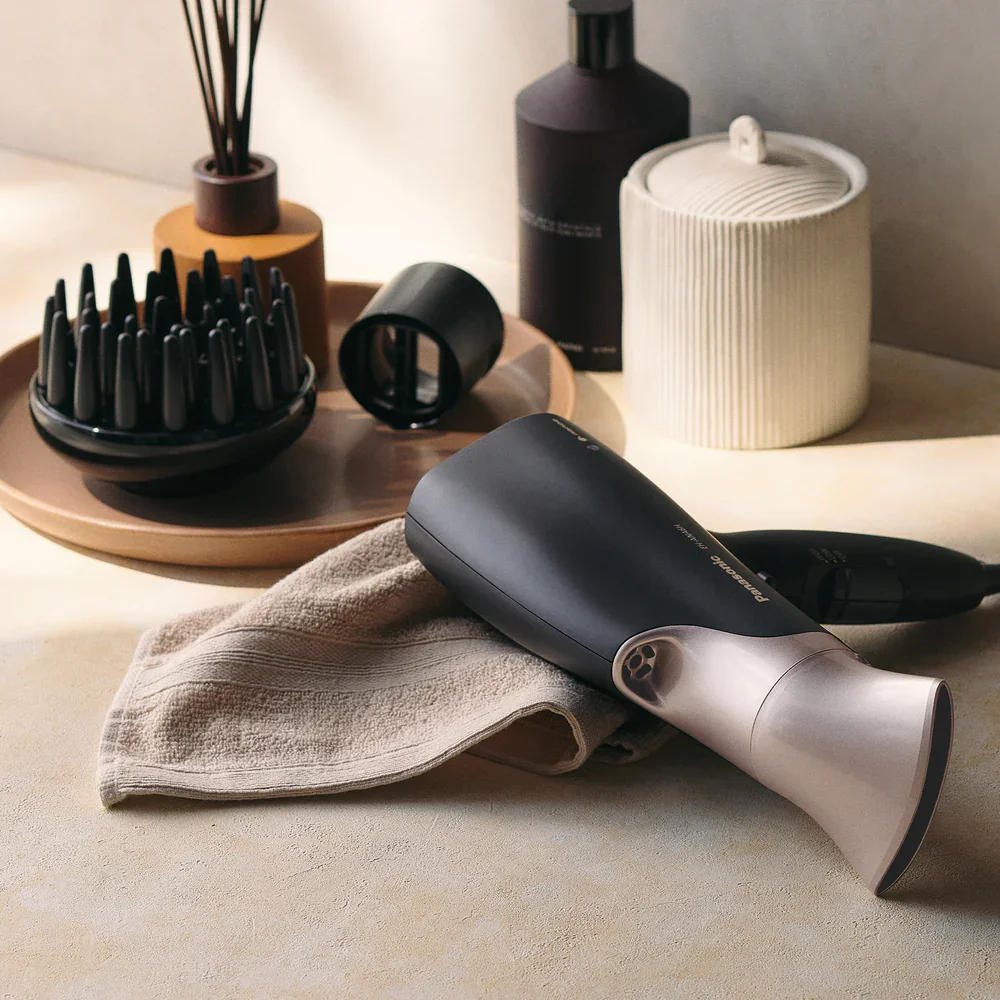 A hairdryer on a beige cloth, surrounded by various grooming and decor items including containers, a diffuser, and a tray with black containers.
