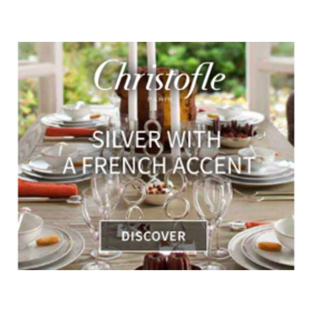Elegant dining table set with white plates, glasses, orange napkins, and a centerpiece, with text promoting Christofle's silver with a French accent.