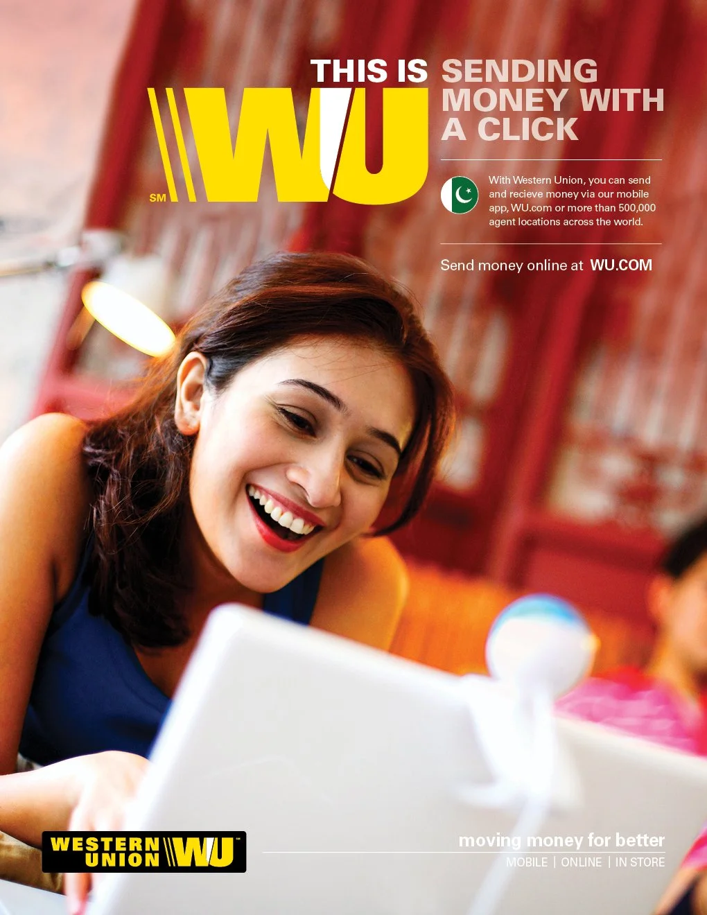A woman with dark hair smiling while looking at a white laptop in a cozy indoor setting, promoting Western Union's online money transfer service.