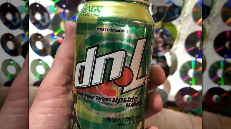 A hand holding a can of 7UP soda in front of a background filled with CDs or DVDs.