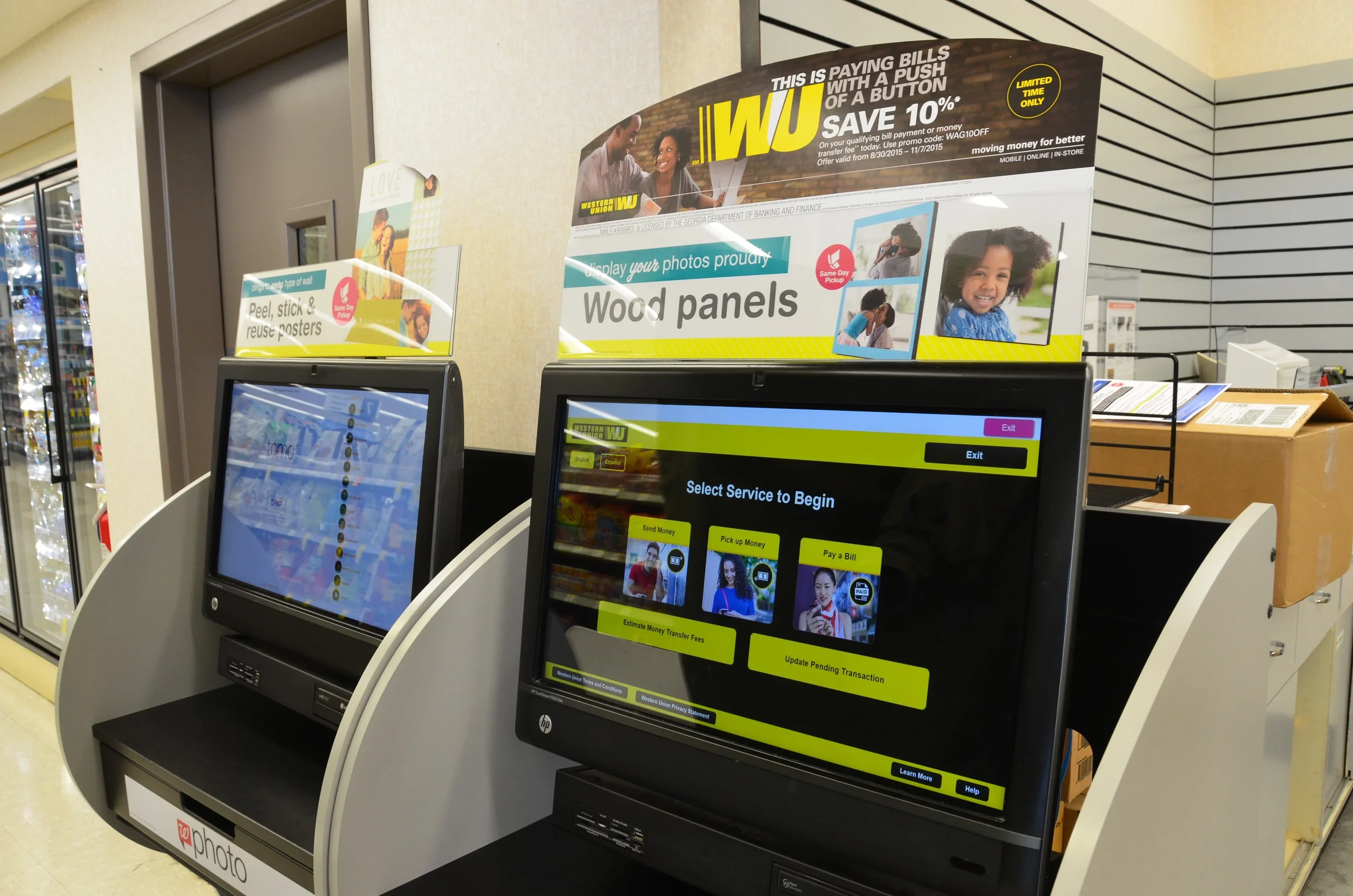 Self-service kiosks for financial transactions in a retail store, with one screen showing options to send money, pick up money, and pay a bill, and promotional signs above advertising wood panels and bill payment services.