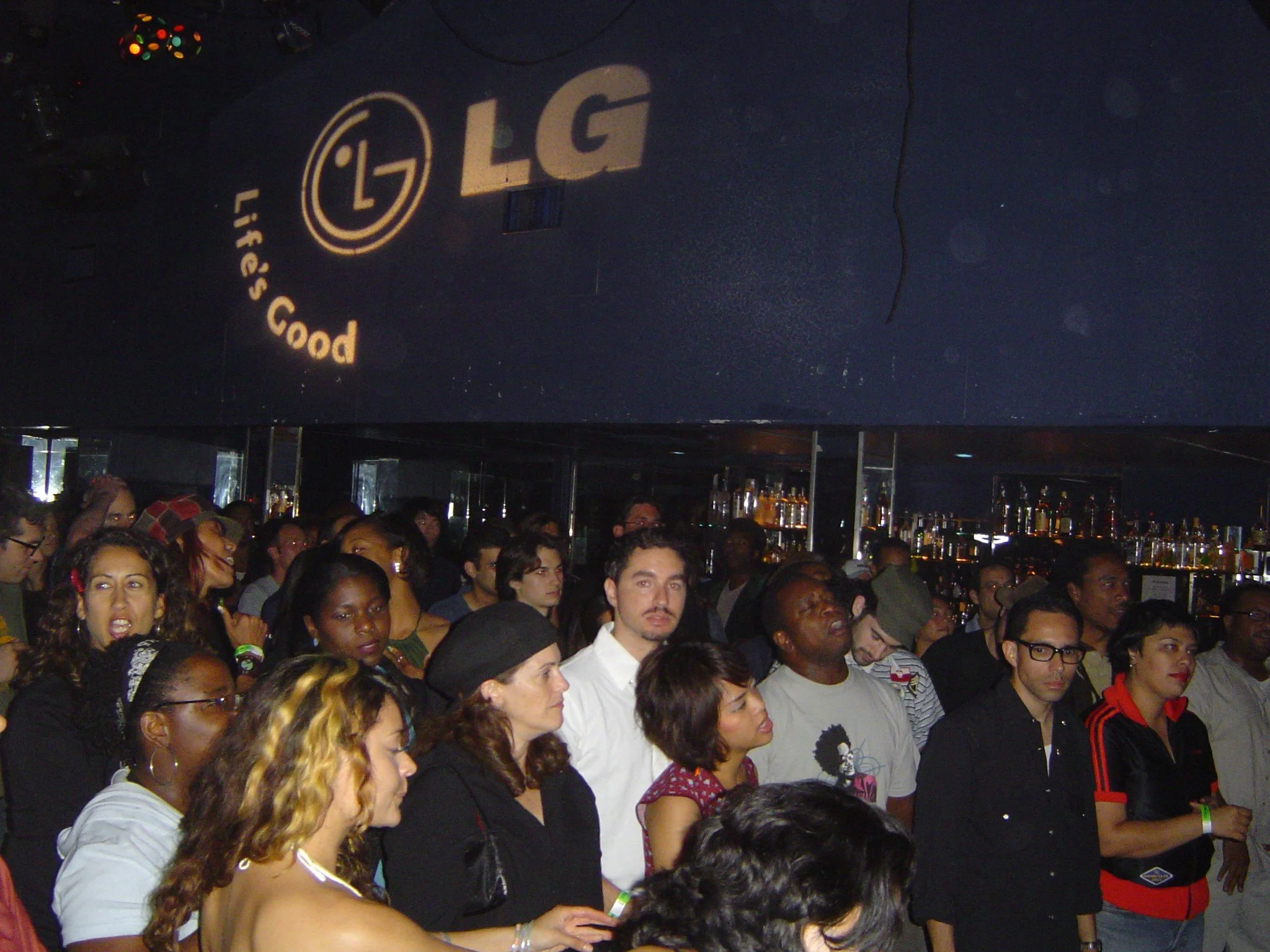 Crowd of people at a bar or nightclub with LG and 'life's good' logo projected on the ceiling.