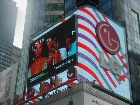Large digital billboard in an urban setting displaying an image of women and the LG logo, with the Love logo and a red and white striped design.