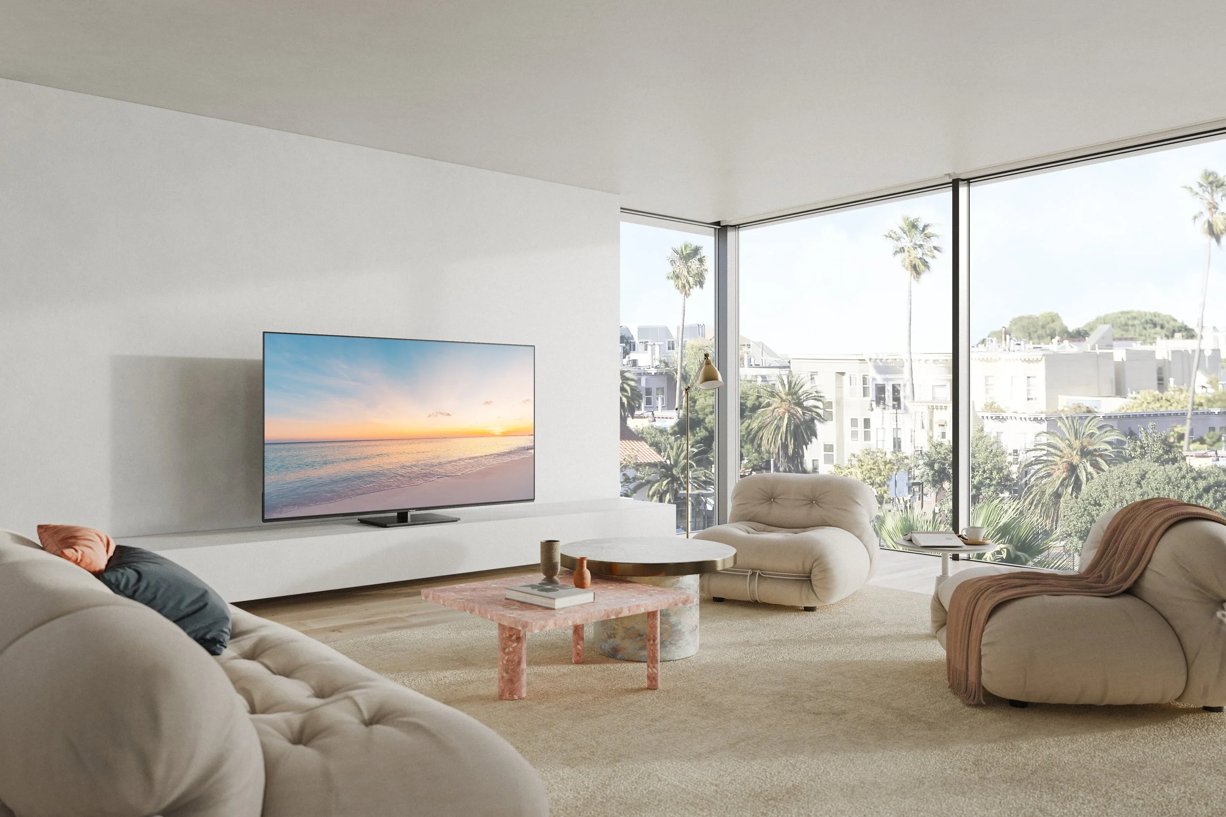 Modern living room with large windows showing cityscape and palm trees, beige tufted sofas, a pink marble coffee table, and a flat-screen TV showing a sunset beach scene.