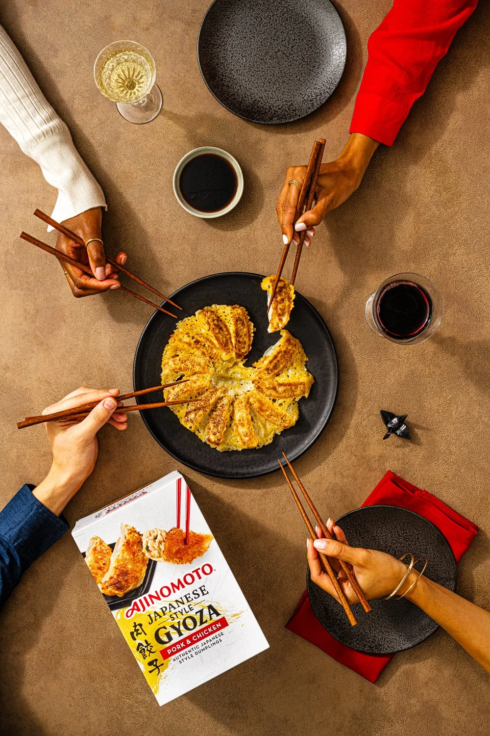 People eating Japanese-style pork and chicken gyoza dumplings with chopsticks at a dinner table.