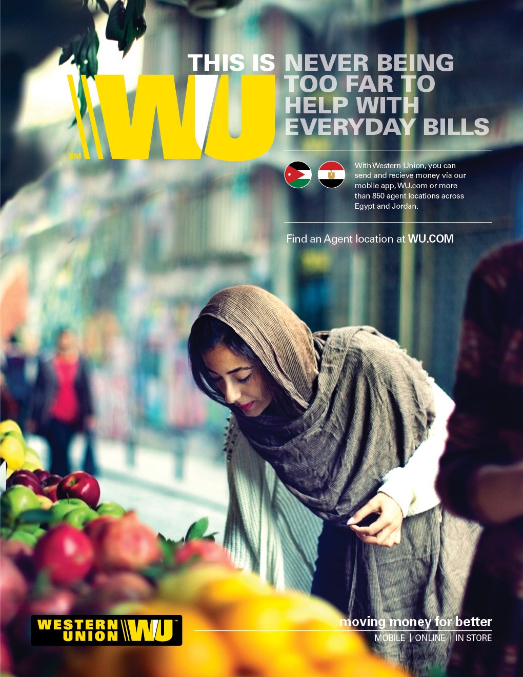A woman wearing a gray scarf and sweater shopping for apples at an outdoor market.