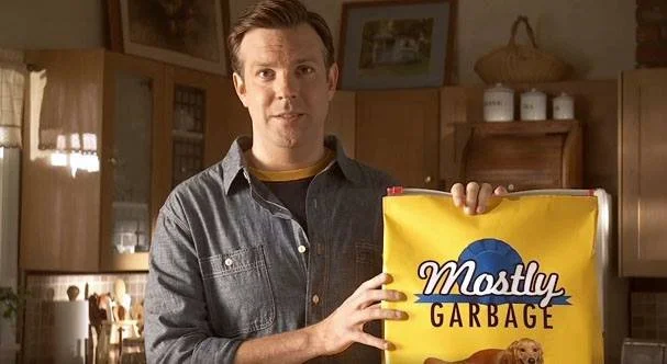 A man holding a yellow bag labeled 'Mostly Garbage' in a kitchen.
