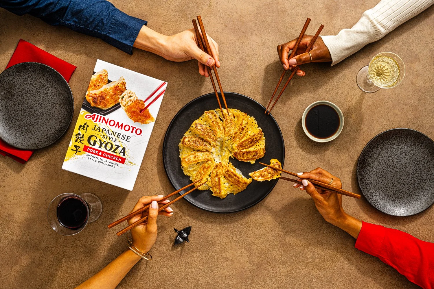 Four people sharing a table with gyoza, soy sauce, and drinks, using chopsticks to serve and eat Japanese-style dumplings.