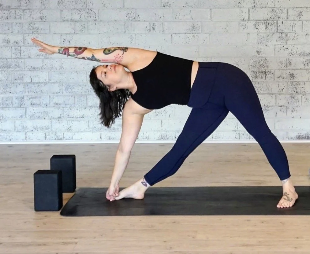 Woman performing a seated twist on a black yoga mat against a white brick wall.