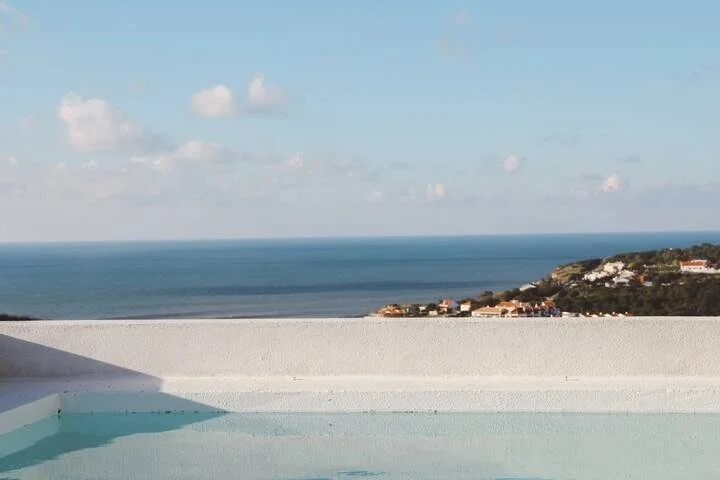 View of the ocean with a small landmass and houses in the distance, seen from a rooftop infinity pool.