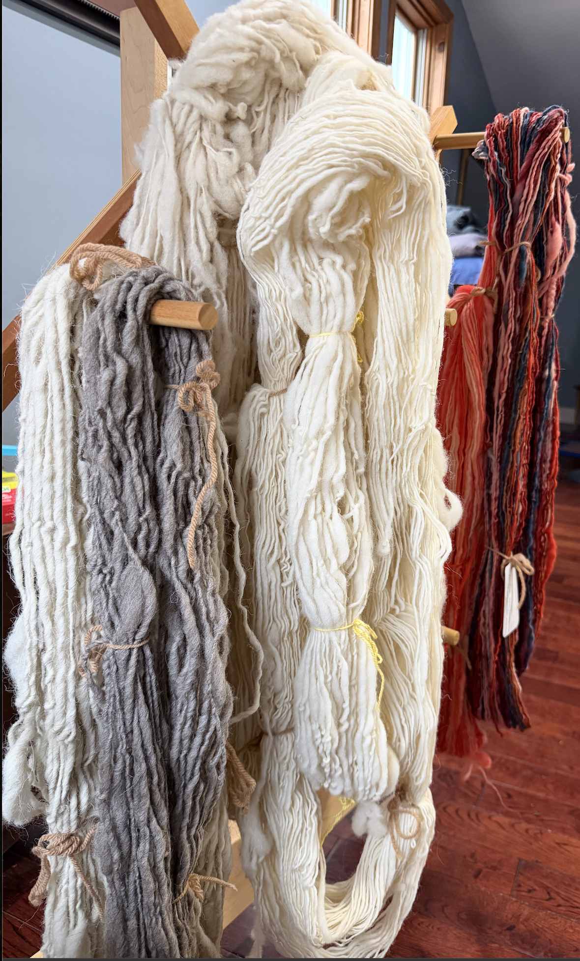 Skeins of different colored wools hanging: natural, grey and multicolored red, pink blue browns