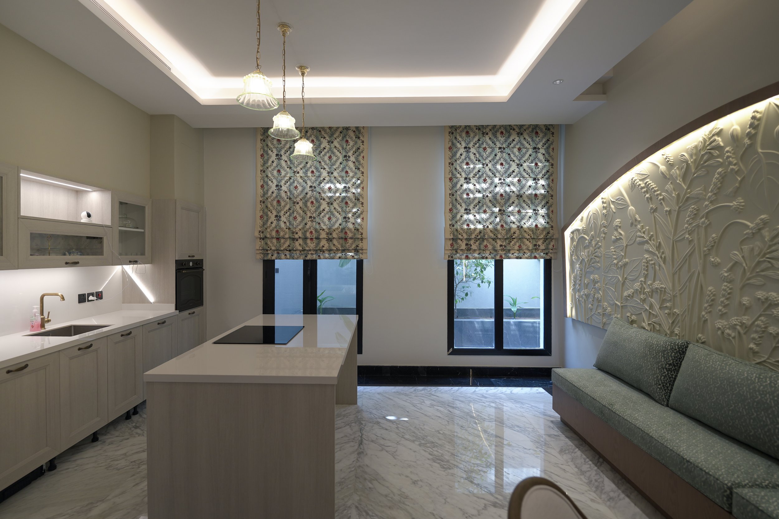 Modern living room with a kitchen island, patterned curtains, marble flooring, and decorative wall paneling with backlighting.
