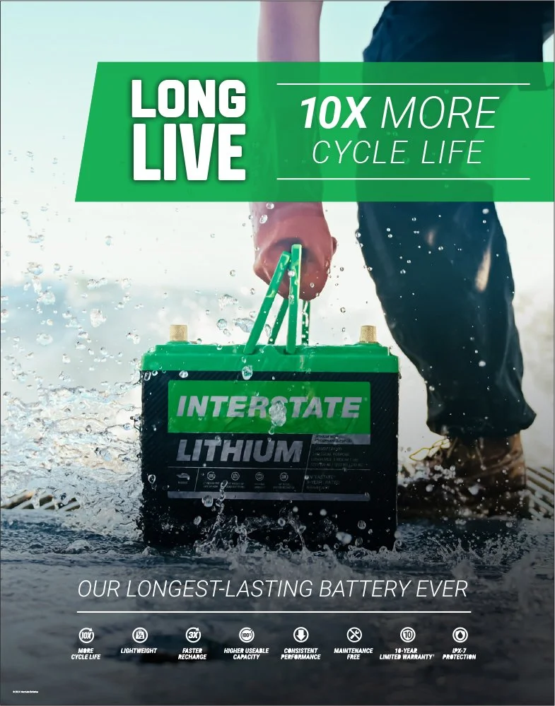 A person in waterproof boots and gloves holding a large Interstate lithium battery while standing in water, with water splashing around. The image promotes a long-lasting, durable battery with features like extended cycle life, lightweight design, fast recharge, high capacity, reliable performance, maintenance-free, a 10-year warranty, and up to 7 protection levels.