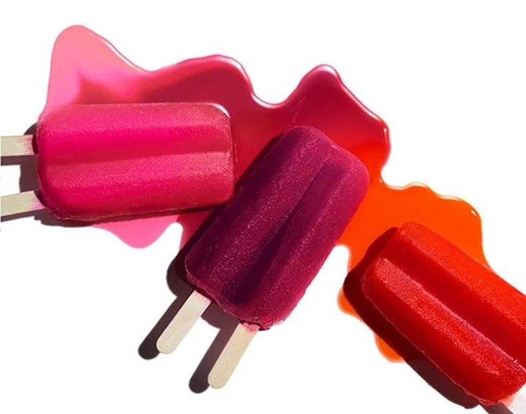 Three colorful popsicles on white background with melted ice cream and syrup.