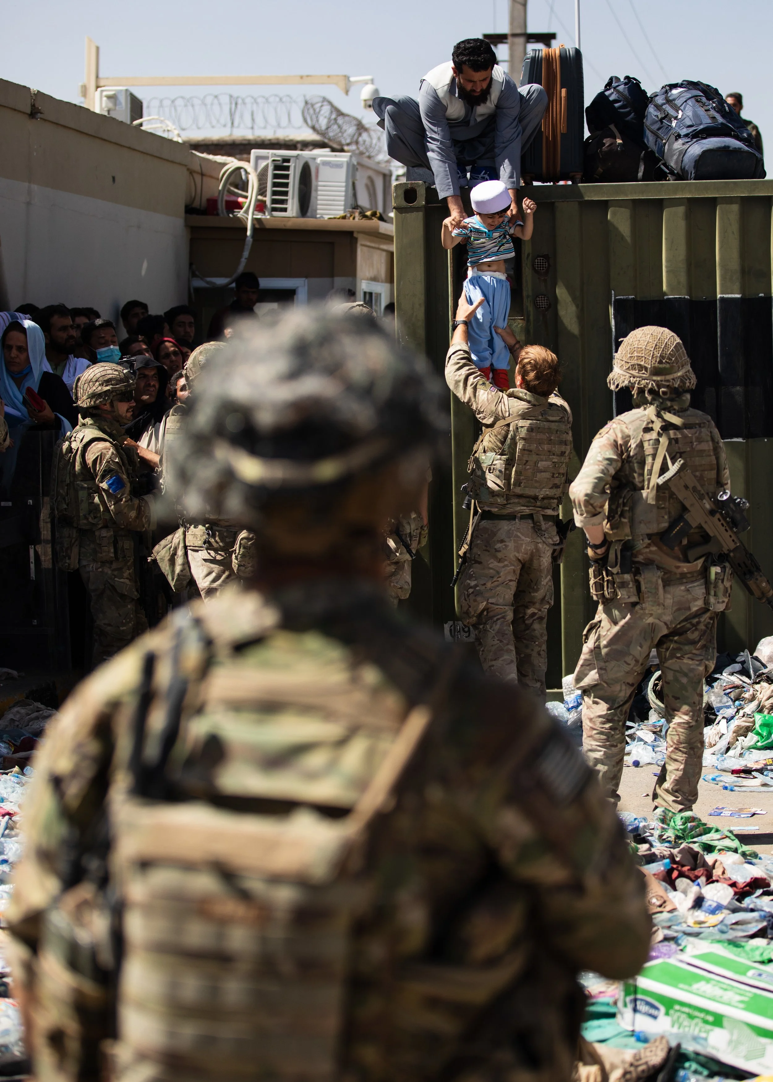 An Afghan man hands his child to a British paratrooper assigned to 2nd Battalion, Parachute Regiment, while a member of 1st Brigade Combat Team, 82nd Airborne Division conducts security at Hamid Karzai International Airport in Kabul, Afghanistan, Aug