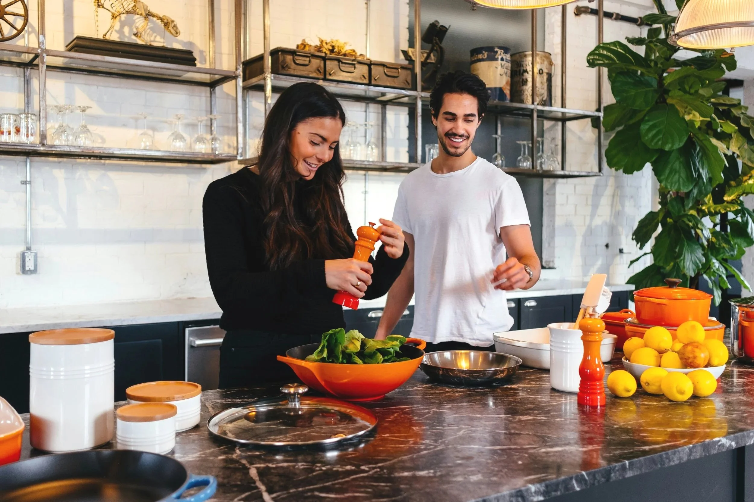 Two people cooking together in a modern kitchen, preparing a meal with vegetables and lemons, smiling and enjoying their time.